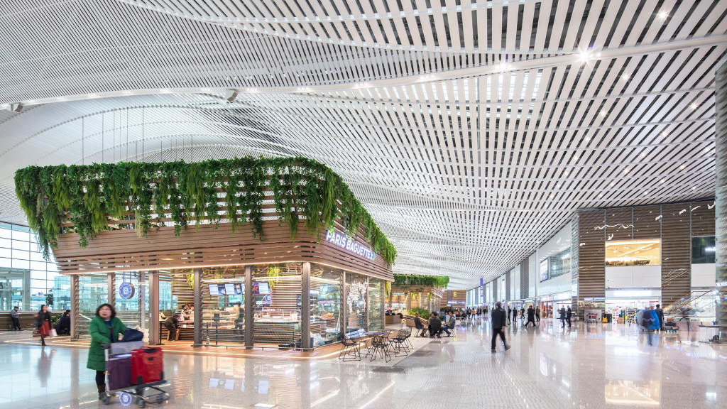 A large glass building with a large glass ceiling and a person pushing a cart with a green plant.
