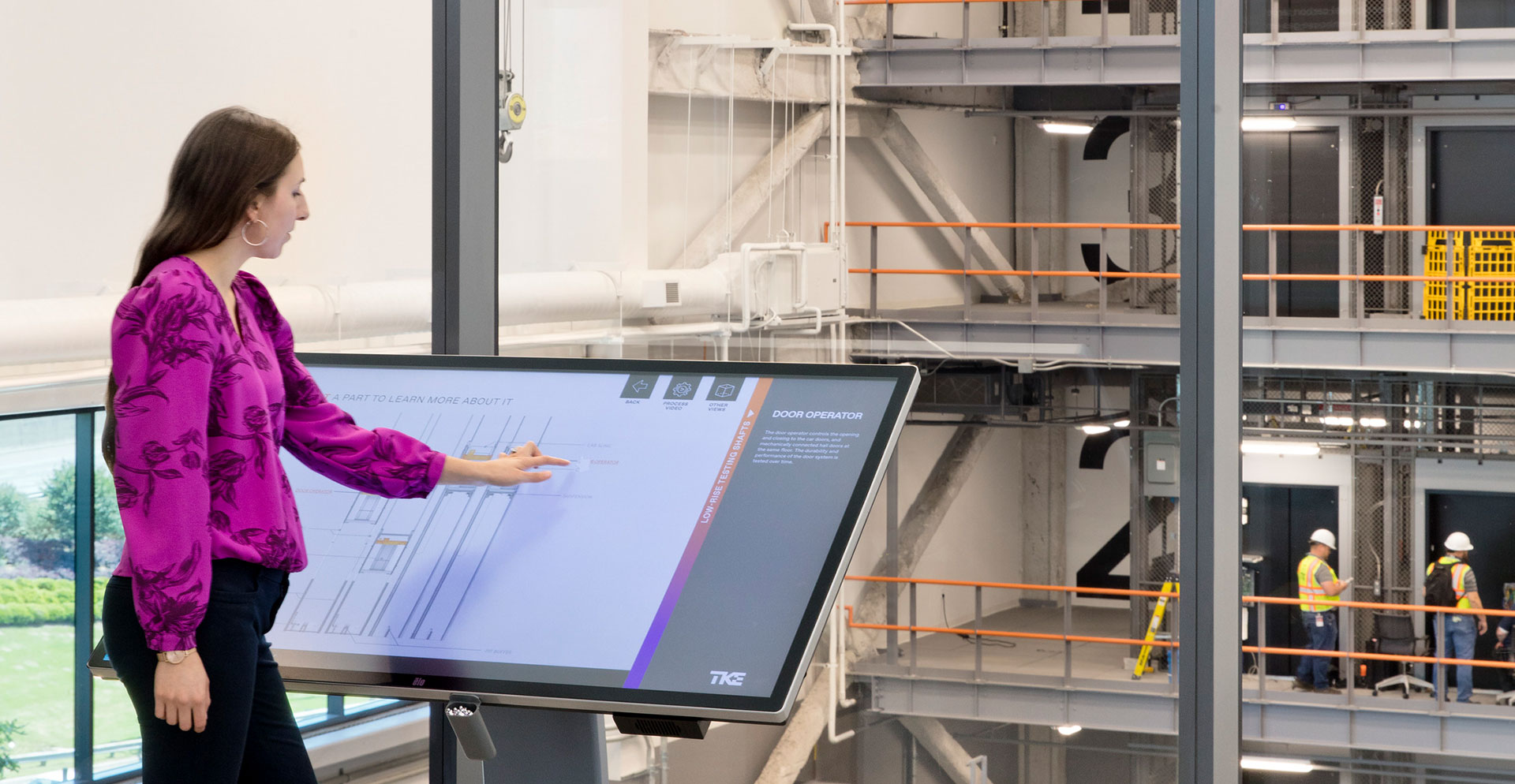 A woman standing next to a large screen.