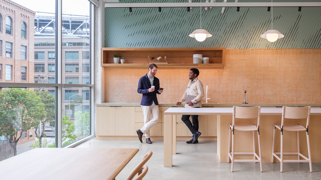 A man and woman sitting at a table in a room with windows.
