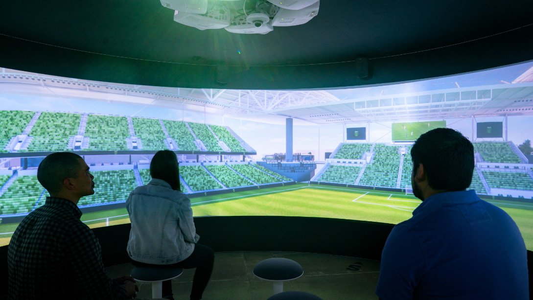 A couple of people sitting in a stadium looking at a football field.