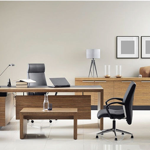 A desk with a laptop and a chair in a room with a white wall.