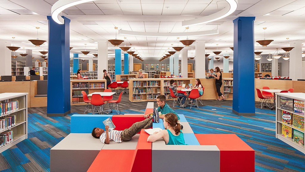 A group of people sitting on a red and white mat in a library.