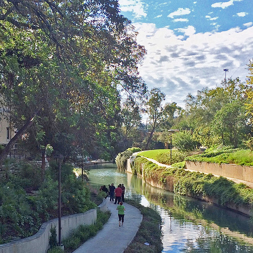 People walking on a path by a river with trees and grass.